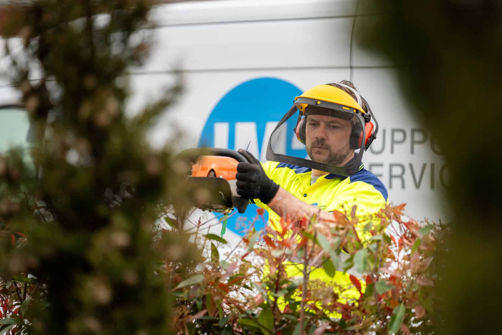 A focused worker in safety gear using a chainsaw to trim vegetation for the JM2 Group.