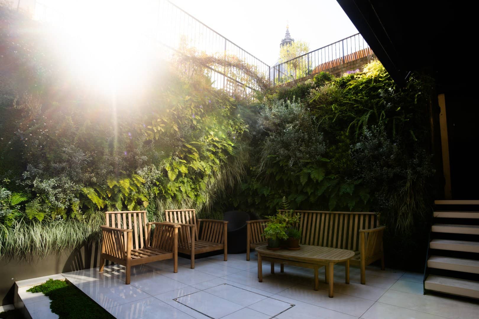 A sunlit patio with wooden chairs and a table, artfully surrounded by lush vertical greenery courtesy of Meristem Design.