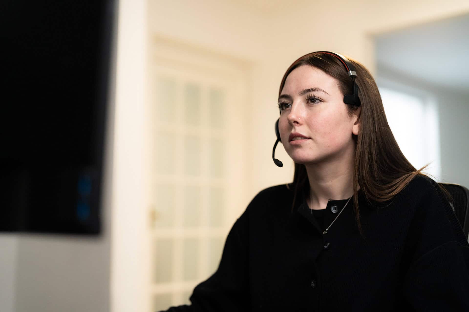 A woman wearing a headset sits at a desk, looking at a computer screen in a bright office environment. | Rubber Duckers