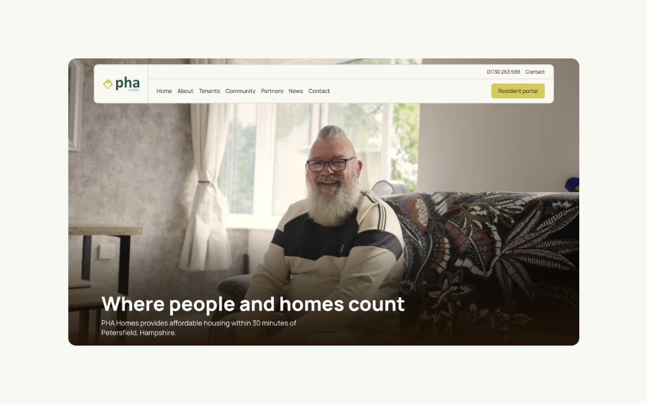 A bearded man sits smiling on a sofa in a well-lit living room. The text reads: "Where people and homes count. PHA Homes provides affordable housing near Petersfield, Hampshire. | Rubber Duckers