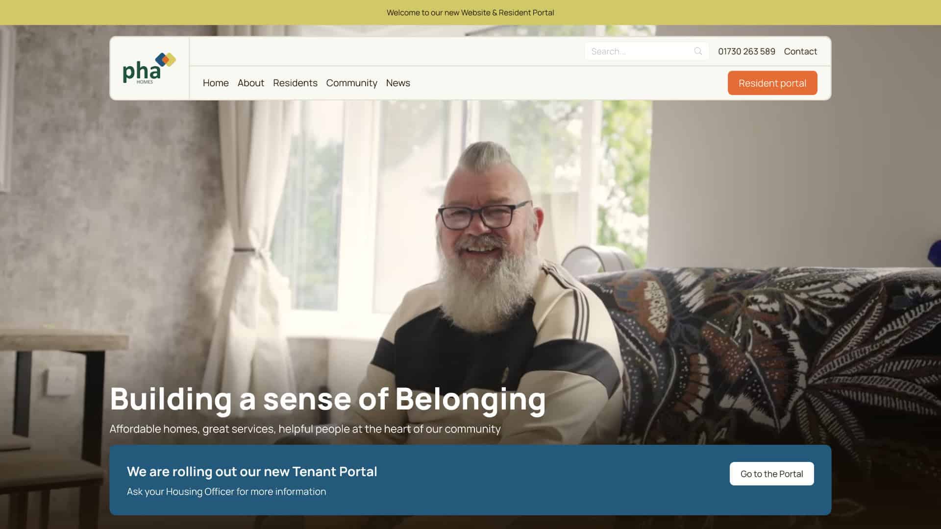 A bearded man with glasses sits smiling in a living room. Website banner text reads, "Building a sense of Belonging" with navigation and a tenant portal button visible. | Rubber Duckers